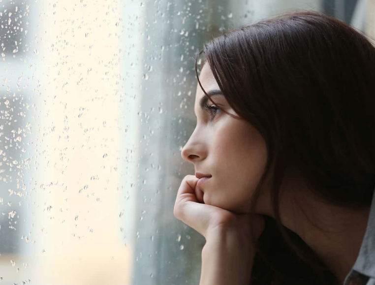 Девушка глядит в окно и грустит